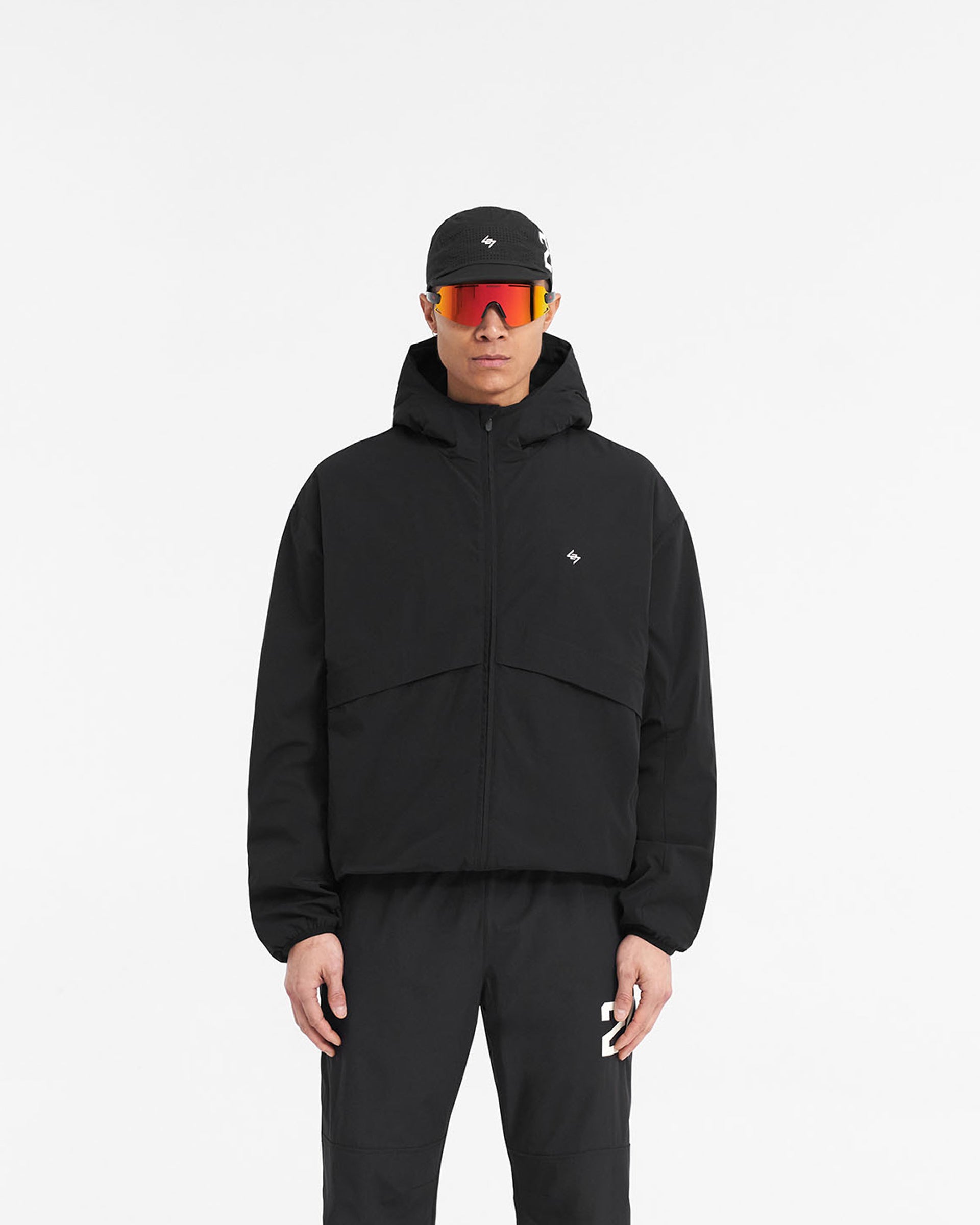 Man wearing a black hooded training jacket on a plain white background | 247 Hooded Training Jacket in Jet Black | Nylon jacket with DWR coating and adjustable hem | 247 Outerwear | Represent Clo